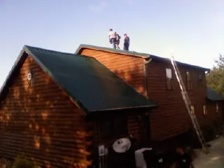 Crew on the ridge of a green metal roof on a two story log home in Jefferson